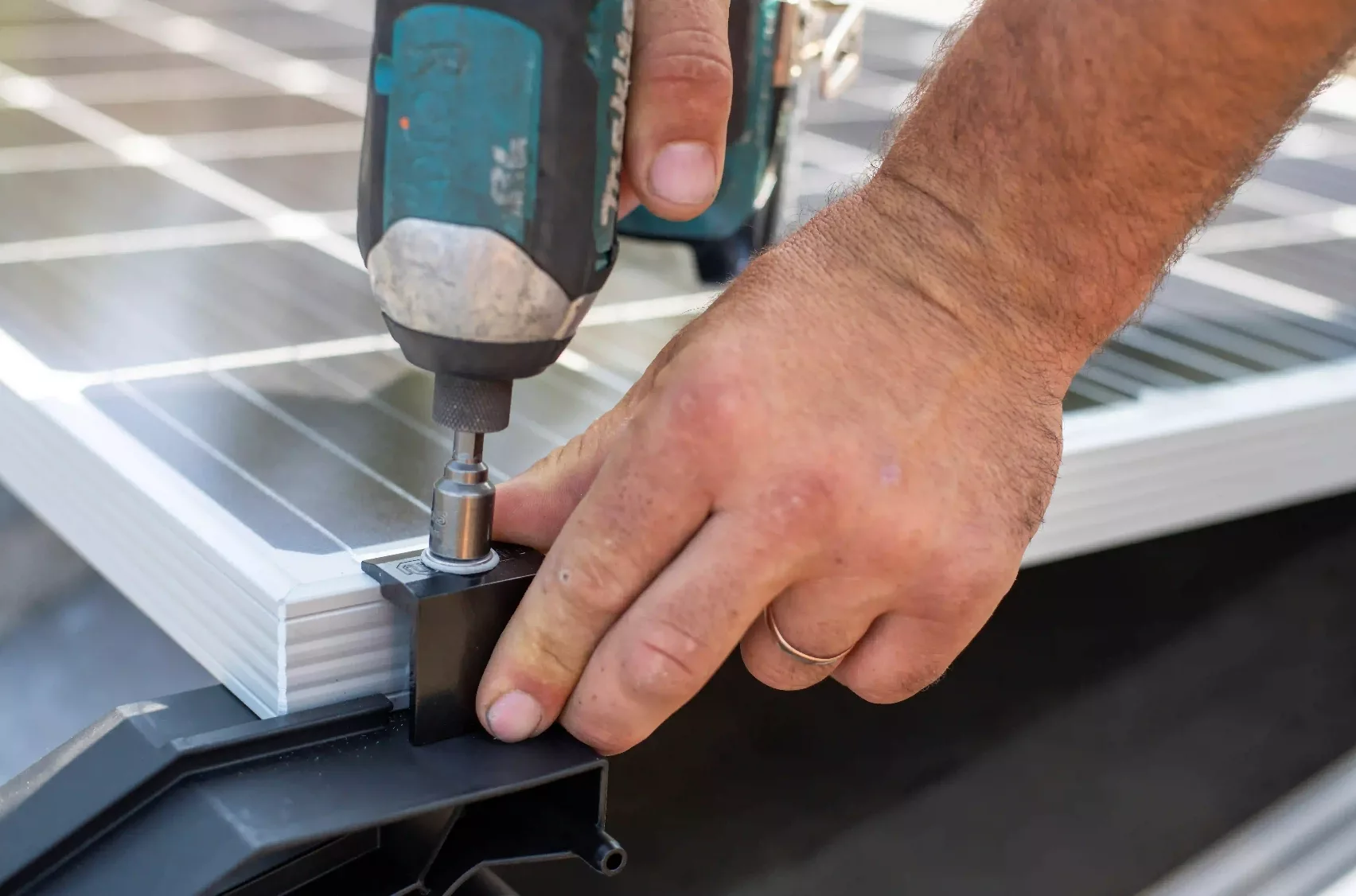 Craftsperson fastening solar panel components with an electric screwdriver.